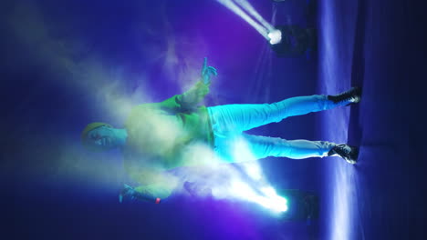 Vertical-video.-Incendiary-funny-Singer-in-yellow-clothes-dancing-and-singing-with-a-microphone-in-neon-color.-Jump-and-move-vigorously.-Hip-hop-and-pop-artist